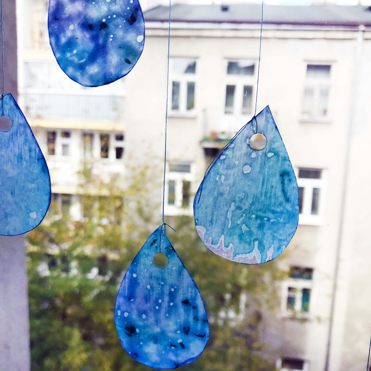 Krople deszczu na tle okna wykonane z papieru i zawieszone na nitce