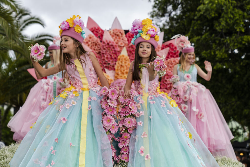 Festiwal kwiatów na Maderze. Dziewczynki w pięknych, balowych sukniach z kwiatami machają radośnie.