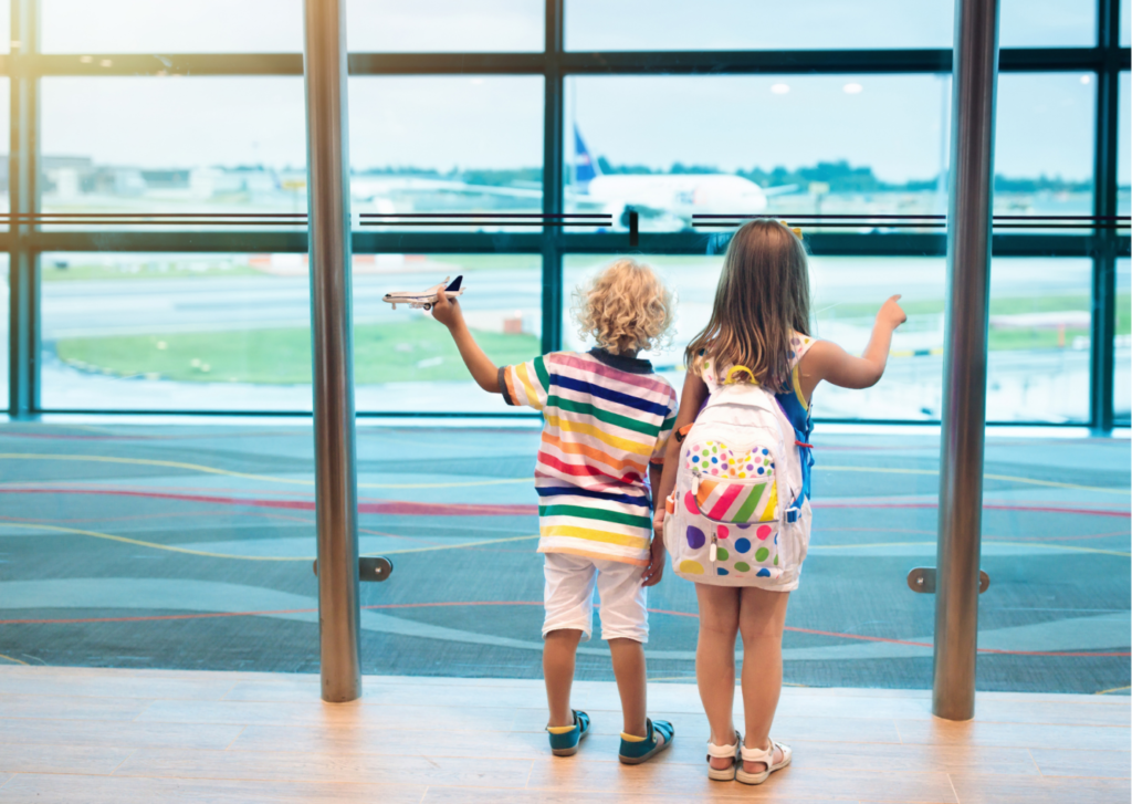 Chłopiec z dziewczynką stoją zwróceni w stronę szyby za którą startuje samolot.