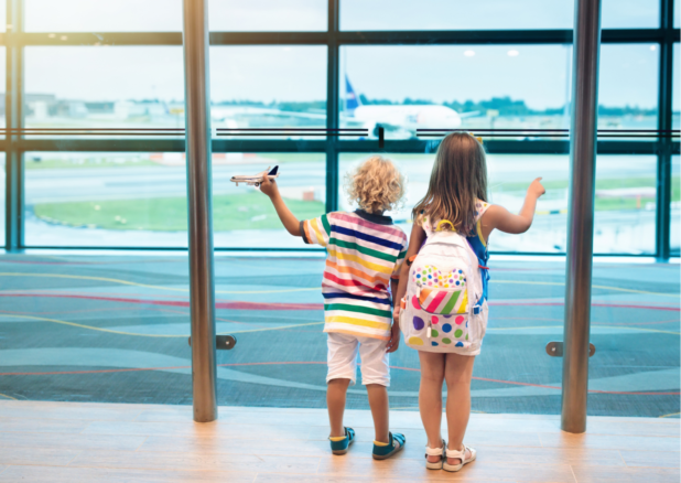 Chłopiec z dziewczynką stoją zwróceni w stronę szyby za którą startuje samolot.