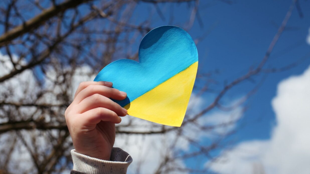Rączka dziecka na tle nieba trzymająca serduszko w barwach flagi ukraińskiej
